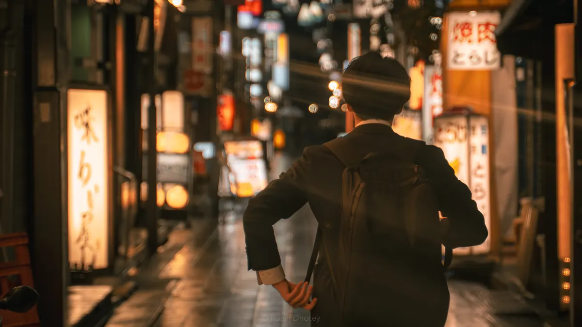 A lone figure standing still in a neon-lit street at night