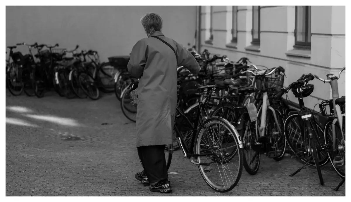 Parked bicycles and a passing figure, in black and white