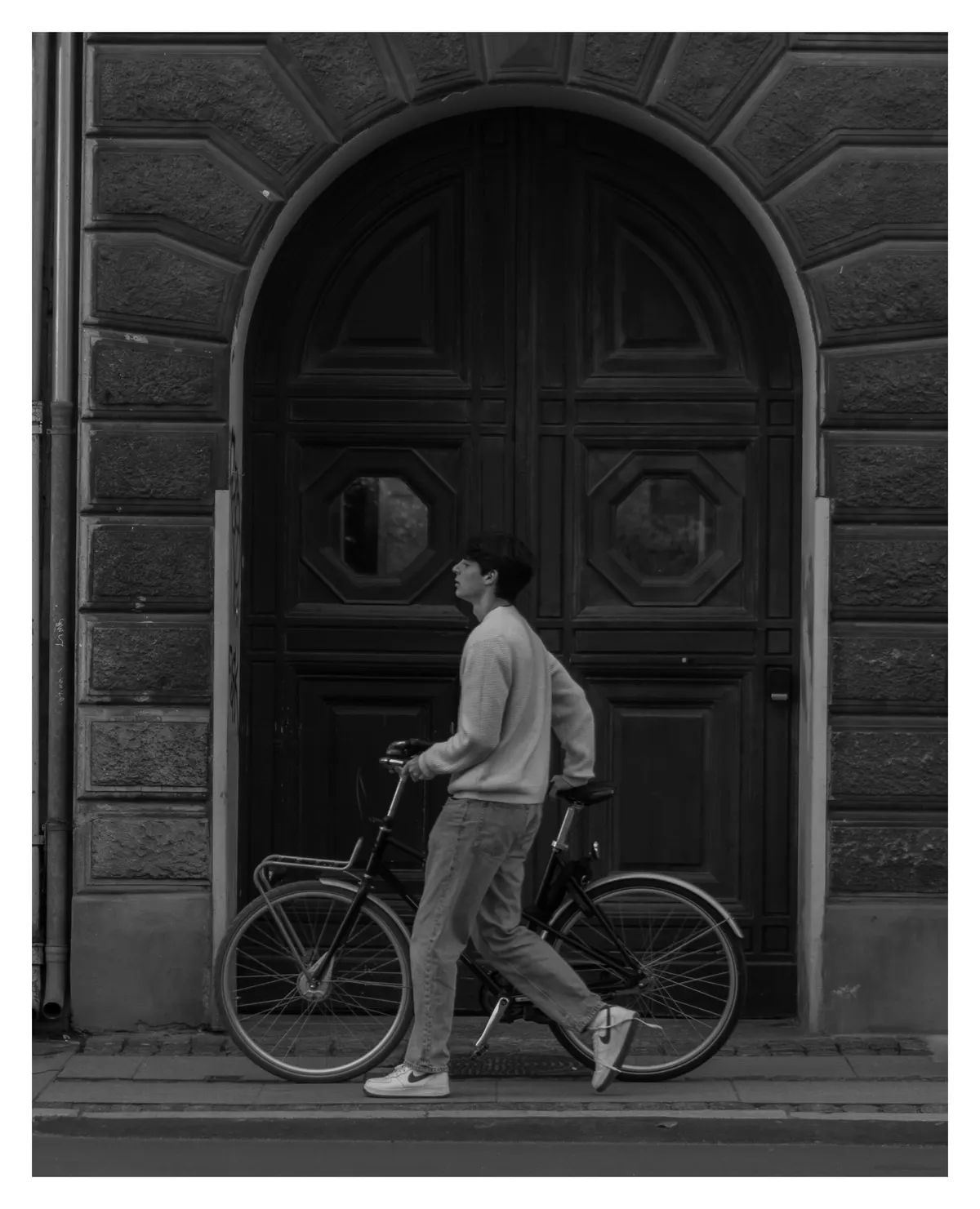 A cyclist passing an arched doorway, in black and white