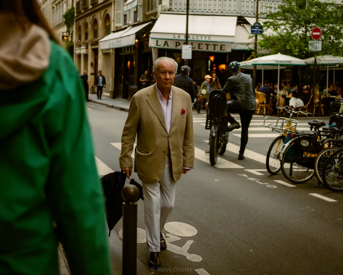 A man in a suit crossing the street, a green coat in the foreground